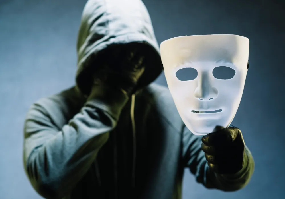 Person iført en hettegenser som holder en maske foran ansiktet – symbolsk bilde som illustrerer den skjulte smerten ved maskert depresjon.