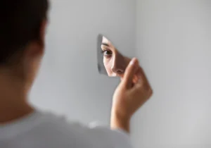 En person med obsessiv-kompulsiv personlighetsforstyrrelse som ser på sitt eget speilbilde i et knust speil, noe som symboliserer indre konflikt og perfeksjonistiske tendenser.