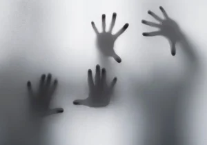 Skygger av hender bak frostet glass symboliserer hvordan stress og traumer kan påvirke psykose – et visuelt uttrykk for indre uro og psykisk kamp.