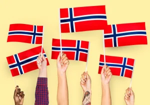 Flere hender holder norske flagg i været mot gul bakgrunn – en illustrasjon av mangfold og nasjonal identitet knyttet til forekomsten av ADHD i Norge.