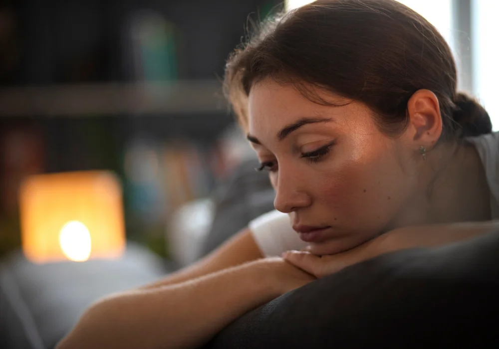 En kvinne med et fjernt blikk som sitter alene i et mørkt rom, illustrerer symptomer på schizoid personlighetsforstyrrelse, som sosial tilbaketrekning.